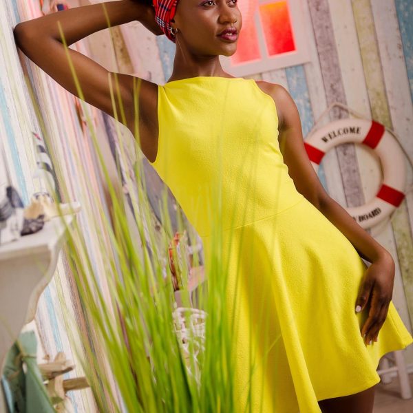 Beauty Shooting in Berlin - Portraitfoto aus einem Fotoshooting eines weiblichen Models mit schwarzem Afro und Kopftuch, in einem gelben Sommerkleid, stehend in einer maritimen Fotokulisse