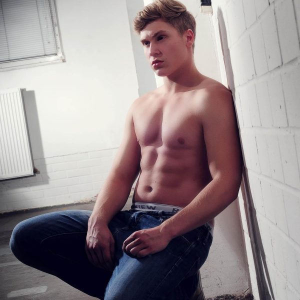 Portraitfoto aus einem Fotoshooting eines männlichen Models mit freiem Oberkörper und Jeans, an eine weiße Brick Wall lehnend